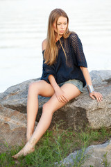 Young pretty woman on stones near water