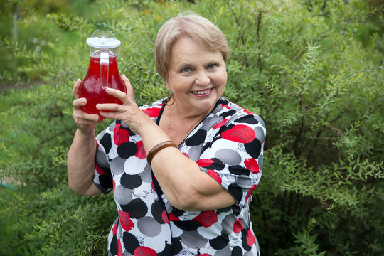 Smiling senior woman showing jug with fresh stewed fruit