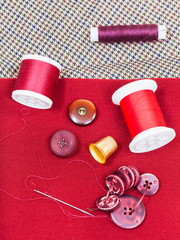 sewing thread, buttons, thimble on red cloth