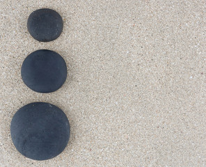 Fototapeta na wymiar Three black zen stones at left side of sand background