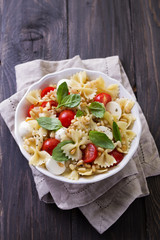 Pasta salad with tomato, mozzarella, pine nuts and basil in a white ceramic bowl on a wooden table