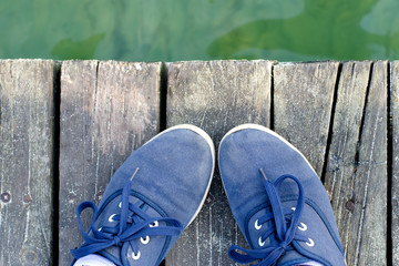 Feet in sneakers standing on the sea dock in summer