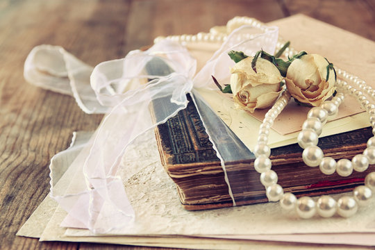 selective focus image of dry roses, white pearls necklace and old vintage books