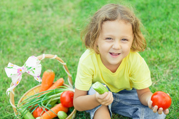 Happy little boy sitting on the grass with a basket of vegetable