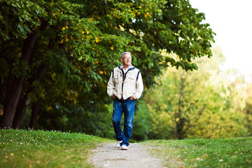 Happy senior man walking and relaxing in park - Powered by Adobe