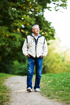 Happy senior man walking and relaxing in park