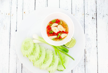 Garlic and pickled chili in fish sauce with cucumber on white wooden background