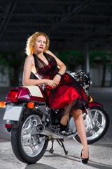 Fototapeta na wymiar Biker girl in dress on a motorcycle over the background of dark