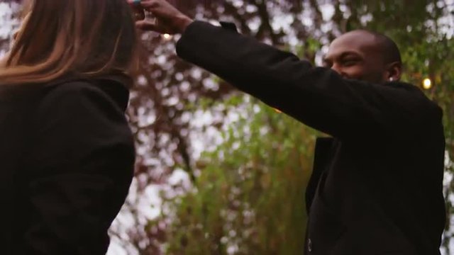 A young man twirls his date as they dance outside, slow motion