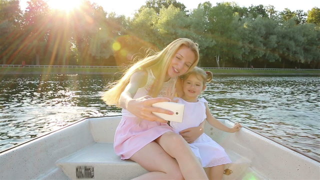 Young attractive mom and her daughter ride on the boat and doing a selfie.