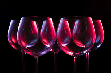 Wine glasses lit by red, blue, lilac nightclub party lights on black background 