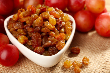 Raisins in bowl with grapes on table close up