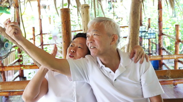 Happy Asian senior couple taking selfie in park on mobile phone