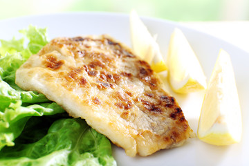 Dish of fish fillet with lettuce and lemon on plate close up