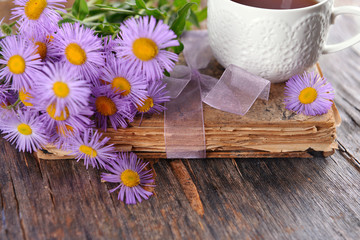 Old book with beautiful flowers and cup of tea on wooden table close up