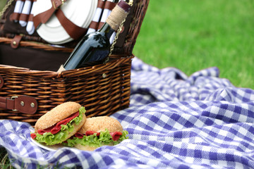 Wicker picnic basket, tasty sandwiches  and plaid on green grass, outdoors