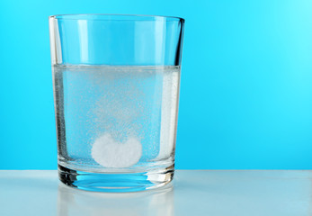 Pill in glass of water on blue background