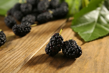 Heap of ripe mulberries with green leaves on table close up