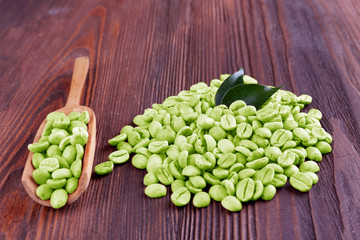 Green coffee beans with leaves and spoon on wooden table close up