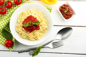 Spaghetti with tomato sauce and cheese on white plate, on color wooden background
