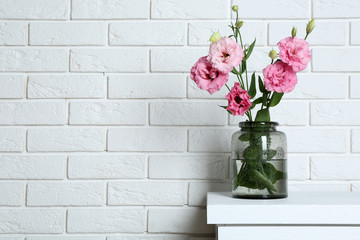 Beautiful flowers in vase on brick wall background