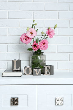 Beautiful flowers in vase with word Love on brick wall background
