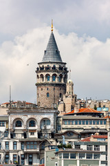 Fototapeta na wymiar View of the Galata Tower in Istanbul, close-up. Turkey. In the foreground, the old houses, the minaret. On the tower are the tourists. Sunny day. Blue sky with clouds.