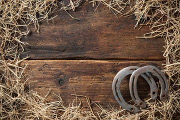 Two old rusty horseshoes with straw on vintage wooden board - obrazy, fototapety, plakaty