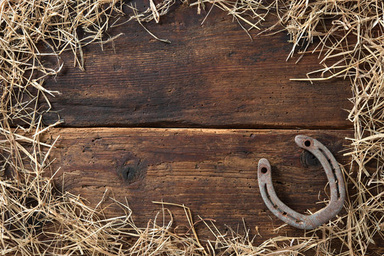 Old rusty horseshoe surrounded by straw on vintage wooden board