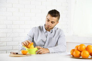 Young man using citrus-fruit squeezer, preparing orange juice