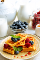 Sweet homemade waffles with forest berries and sauce on table background
