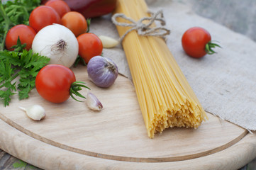 Pasta spaghetti, onion, garlic and tomato on wooden background