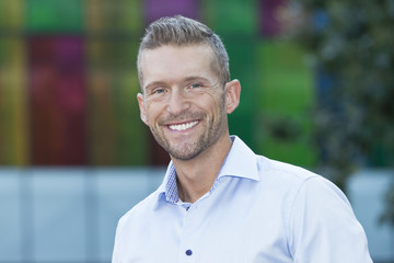 Mature Man Smiling At The Camera. He is outside of the office.