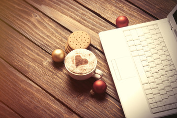 Cup of coffee with heart shape and laptop computer