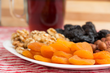 Healthy collection of dried fruits - apricot , plums, walnuts, and hazelnuts in a white plate with a drink
