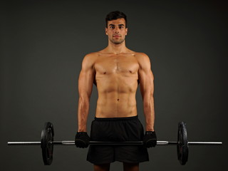 Fototapeta na wymiar Athlete young man exercises with big dumbbell on gray background