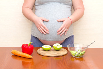 Obraz na płótnie Canvas Pregnant woman and healthy food. Vegetables and fruit on the table against the background of the pregnant woman. Prenatal diet.