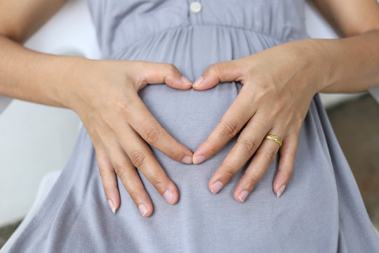 Pregnant women put his hand on her belly to heart shape.