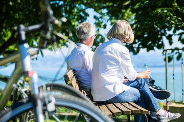 Senior Frau und Mann bei Pause auf Fahrradausflug sitzen auf einer Bank
