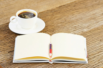 Notebook and  coffee in white cup on wooden table