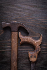 Rusty handsaw and claw hammer on vintage wooden background