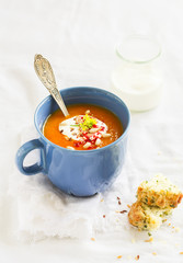pumpkin soup served in blue ceramic mug with cream and paprika on a light wooden background