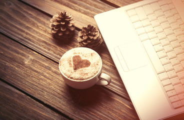 Cup of coffee with heart shape and laptop computer