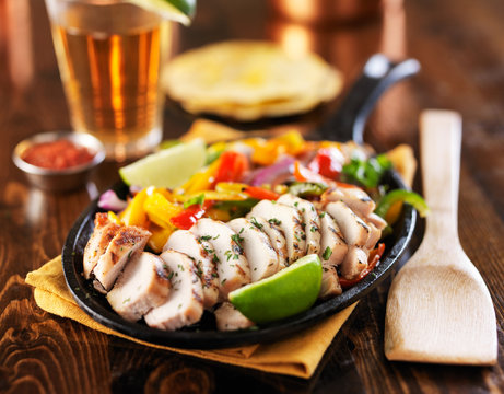 grilled mexican chicken fajita skillet meal on wooden table top with beer in background