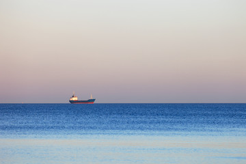 Small lonely ship floating on flat surface of sea on calm morning.