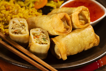 Portion baked spring rolls with vegetables and rice on a plate.