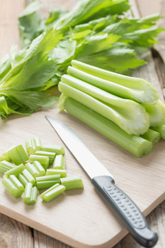 Celery chopped on wooden cutting board with knife.