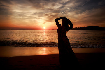silhouette of slim girl in long against sunrise over sea