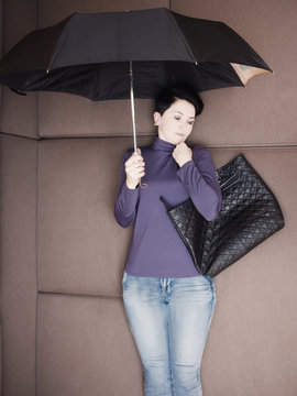 Sad businesswoman lies with umbrella and her handbag on sofa