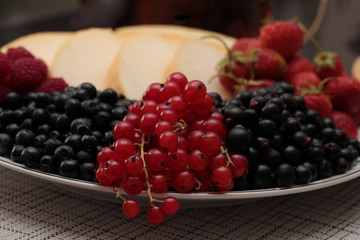 A plate of fruits and red currants on the foreground
